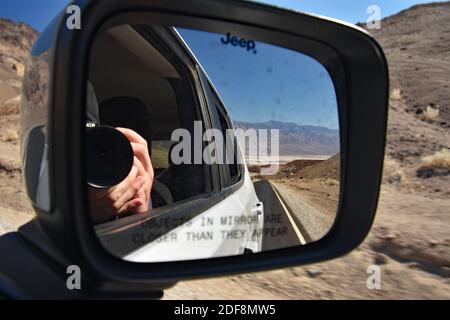 Un maschio bianco scatta una foto dello specchio a forma di ala su un'auto e si riflette in essa mentre si guida lungo Artists Drive nel Death Valley National Park, USA. Foto Stock