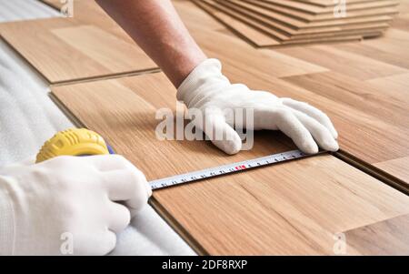 Installazione del pavimento laminato, dettaglio sulle mani dell'uomo in guanti bianchi che tengono il nastro di misurazione su piastrelle di legno Foto Stock
