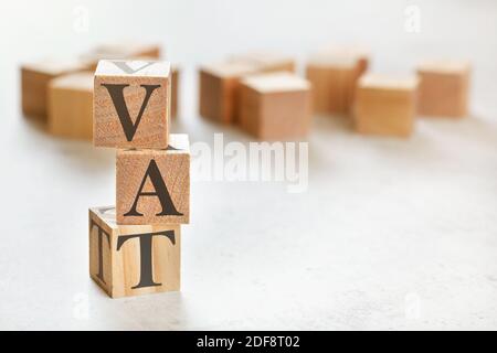 Tre cubetti di legno con lettere IVA (significa imposta sul valore aggiunto), su tavola bianca, più sullo sfondo, spazio per il testo nell'angolo destro in basso Foto Stock