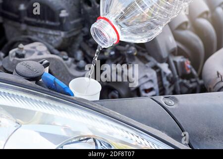 Versando acqua distillata (alternativa ecologica al liquido di lavaggio) alla vasca di lavaggio in auto, dettaglio sul flusso di liquido trasparente che scorre Foto Stock