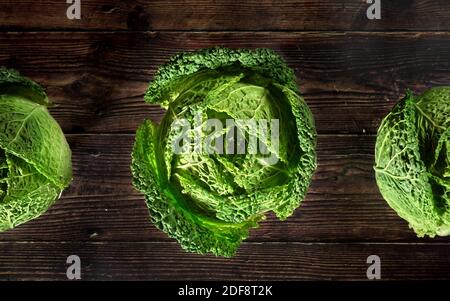 La lattuga verdeggiante sabauda si dirige su una tavola di legno scuro, vista dall'alto Foto Stock