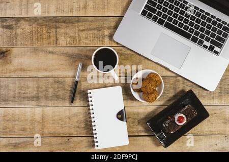 Laptop, diario, torta di butterscotch e tazza di caffè su legno rustico. Disposizione piatta. Foto Stock