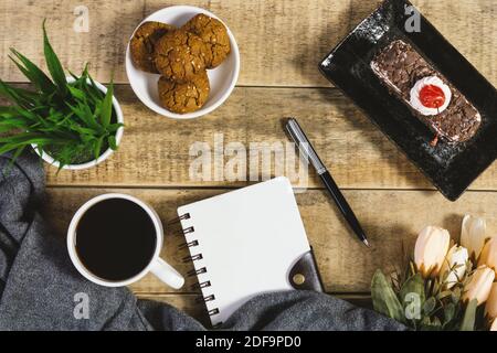 Diario, biscotti e tazza di caffè su legno rustico. Disposizione piatta. Foto Stock