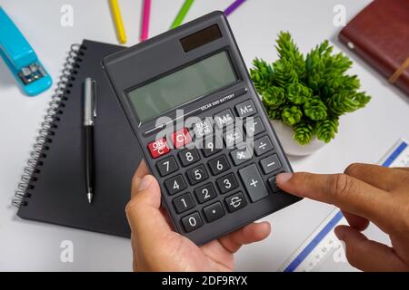 Mani che tengono una calcolatrice sulla parte superiore del tavolo di lavoro dell'ufficio. Foto Stock