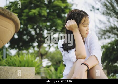 Triste giovane donna asiatica seduta in un parco. Foto Stock