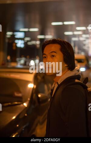 Uomo asiatico in attesa di un giro in auto di notte in aeroporto. Foto Stock