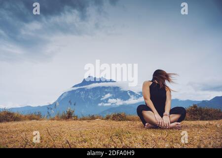 Donna seduta e giocosamente oscillare i capelli con vista del Monte Kinabalu sullo sfondo. Foto Stock