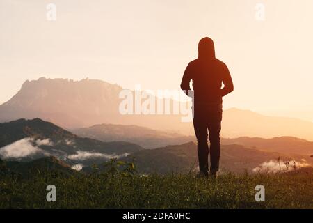 Vista della silhouette uomo da dietro in piedi guardando lontano al Monte Kinabalu all'alba. Foto Stock