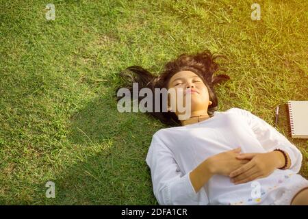 Giovane ragazza asiatica sdraiata sull'erba nel parco e godendo il momento della pace. Foto Stock