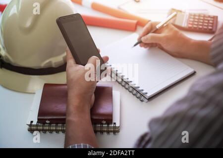 Uomo che scrive su blocco note e usa il telefono. Concetto di gestione dei progetti. Foto Stock