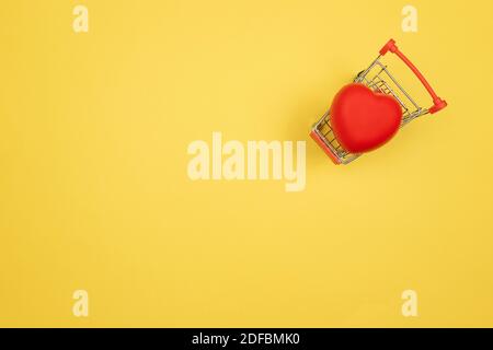 Un cuore rosso si trova in un carrello per lo shopping su sfondo giallo. Concetto di San Valentino Foto Stock