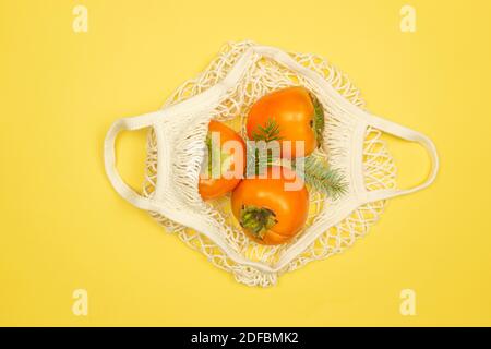 I frutti di persimmon si trovano nel sacchetto di maglia bianca su uno sfondo giallo. Concetto di cibo sano Foto Stock