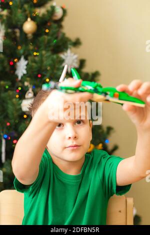 Gioco di ragazzo con pterodattile fatto da blocchi di plastica. Albero di Natale in background. Mettere a fuoco sul viso dei bambini Foto Stock