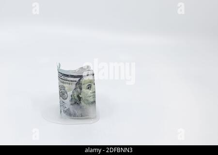 Fusione lenta di banconote da 100 dollari congelate in un cubetto di ghiaccio su sfondo bianco con spazio per la copia. Concetto di attività congelate, economia congelata, freddo Foto Stock
