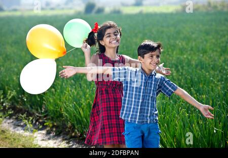 Felice fratello e sorella che si diverte con palloncini in agricoltura campo Foto Stock