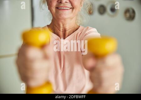 Donna anziana allegra che fa esercizio con manubri a casa Foto Stock