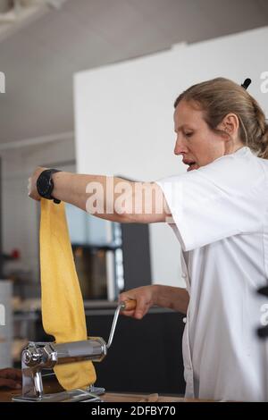 Senior caucasico femmina chef lavorazione foglio di pasta in macchina a. cucina ristorante Foto Stock