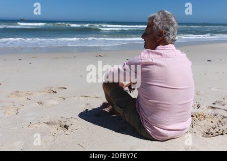 Uomo caucasico anziano seduto sulla spiaggia vicino al mare Foto Stock