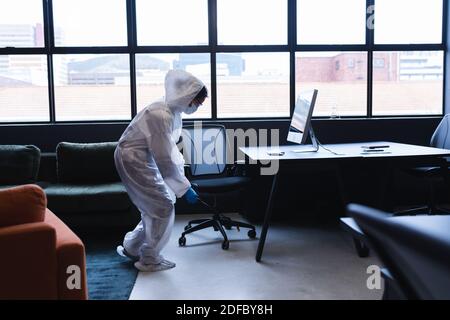 Operatore sanitario in abbigliamento protettivo disinfettante spray in ufficio Foto Stock