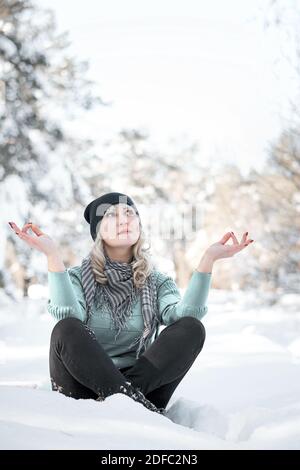 Bella donna si siede in posizione yoga in foresta ghiacciata. La signora medita nel parco invernale. Foto Stock