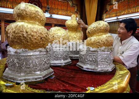 Myanmar (Birmania), uomo al tempio sul lago Inle mettendo foglia d'oro su statue di Buddha Foto Stock