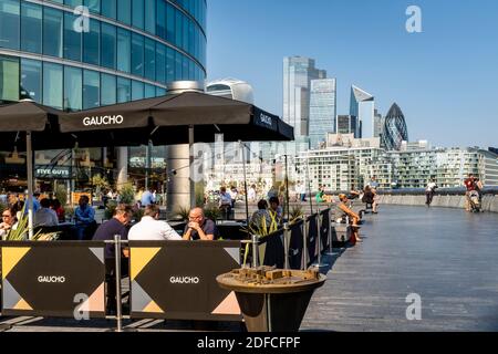 La gente mangia all'aperto al ristorante Gaucho (Tower Bridge) con la City of London nel Backround, London Bridge City Area, Londra, Regno Unito. Foto Stock