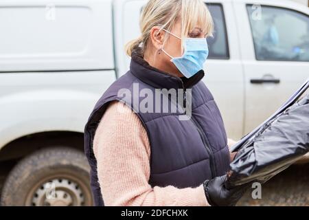 Gestore pacchi di un servizio di consegna con maschera facciale controlla la consegna prima della consegna Foto Stock