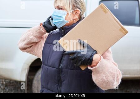 Gestore pacchi di un servizio di consegna con maschera facciale chiama il destinatario per accettare il pacco Foto Stock