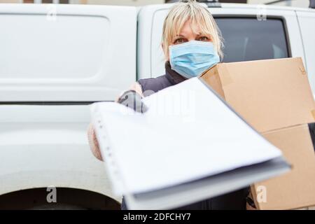 Il trasportatore di pacchi di un servizio di consegna indossa una maschera facciale A causa di Covid-19 e chiede una firma Foto Stock