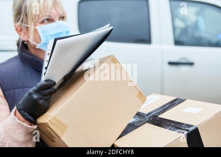 Gestore pacchi per un servizio di consegna con maschera facciale durante la consegna dei pacchi Foto Stock