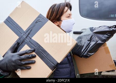 Gestore pacchi di un servizio di consegna con maschera facciale effettua molti pacchi per la consegna Foto Stock