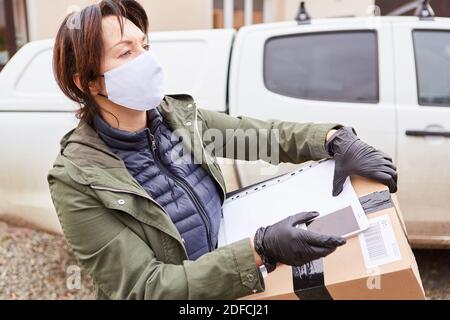 Gestore pacchi di un servizio di consegna con maschera facciale consegna il pacco e guarda intorno Foto Stock