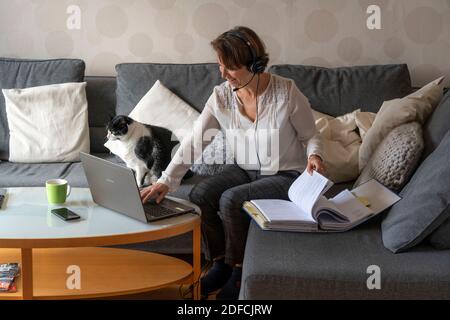 Donna, metà degli anni '50, lavora da casa, con un computer portatile e comunica con i colleghi, l'ufficio di casa, sul divano, Foto Stock