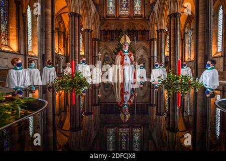 Il chorister Sebastian Kunzer, 13 anni, si trova accanto al fonte battesimale, circondato dai suoi compagni cantori della cattedrale, mentre si abitua a indossare le vesti del vescovo mentre prova il suo ruolo di chorister Bishop alla Cattedrale di Salisbury nel Wiltshire. Durante l'evento annuale, che si svolge intorno al giorno di San Nicola, un coro è scelto per agire come vescovo per un breve periodo in avvento in una consuetudine medievale di inversione di ruolo, in cui maestri e servitori scambiano posti per un incantesimo. Foto Stock