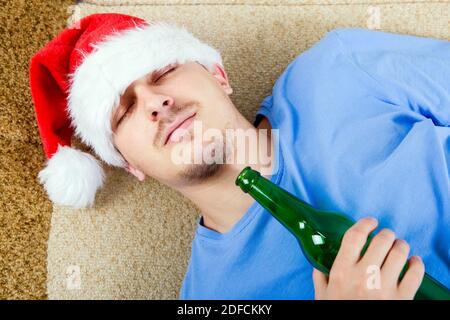 Un uomo a Santa Hat che dorme sul divano con Una birra Foto Stock