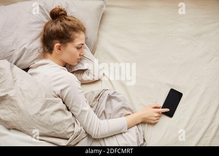 Giovane donna che spegne il suo telefono cellulare mentre si sdraiava il suo letto al mattino Foto Stock