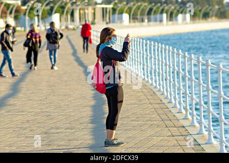 Huelva, Spagna - 3 dicembre 2020: Una donna non identificata che scatta una foto con il suo telefono cellulare al tramonto sulla passeggiata di Huelva Foto Stock