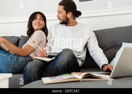 Immagine del libro piacevole di lettura della coppia bella e di lavoro con computer portatile mentre sei seduto sul divano di casa Foto Stock