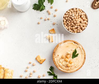 Flatlay Hummus in un piatto di legno e ceci crudi in una ciotola. Piatti di ceci, un piatto vegetariano. Spazio di copia. Foto Stock