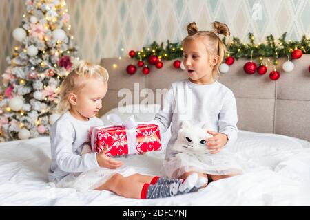 Due sorelle carine delle ragazze con i regali di Natale siedono sul letto A casa in camera decorata a Natale Foto Stock