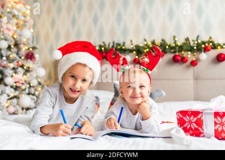 Due sorelle carine delle ragazze con il presente di Natale stanno sopra Letto a casa in camera decorata a Natale e sorridere guardando alla telecamera Foto Stock