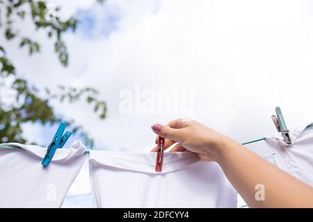 La mano delle donne appende fuori la lavanderia su una corda, con il cielo nuvoloso sullo sfondo. Foto Stock