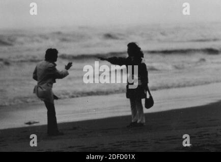 Anni '60 anni '70 mare aperto giovane coppia in bianco e nero divertirsi alla spiaggia toscana di Castinglioncello. Italia. Scansione di graffi e difetti Foto Stock