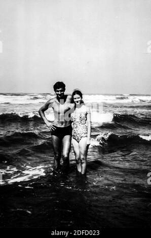 Anni '60 anni '70 mare aperto giovane coppia in bianco e nero divertirsi alla spiaggia toscana di Castinglioncello. Italia. Scansione di graffi e difetti Foto Stock