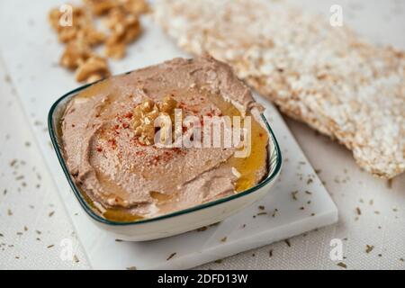 primo piano di una ciotola con un hummus appetitoso, fatto con ceci, noce e rosmarino, su un tavolo, accanto ad alcune torte di riso soffiato Foto Stock