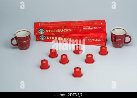 Tazze da caffè Starbucks accanto alla macchina Nespresso. Varietà di tazze di marca per le vacanze dietro le capsule di alluminio utilizzate per fare gocciolare il caffè. Foto Stock