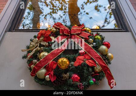 Corona di Natale tradizionale fatta da rami di abete verde e baubles dorati con arco di nastro rosso. Decorazioni di benvenuto per le vacanze Foto Stock
