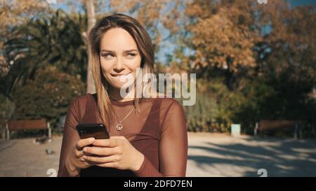 Ritratto di bella ragazza bionda flirty che guarda via mentre sms con il ragazzo nel parco Foto Stock