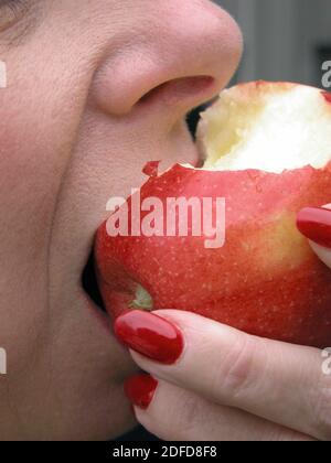 Donna che prende un morso da una mela rossa deliziosa Foto Stock