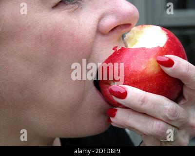 Donna che prende un morso da una mela rossa deliziosa Foto Stock